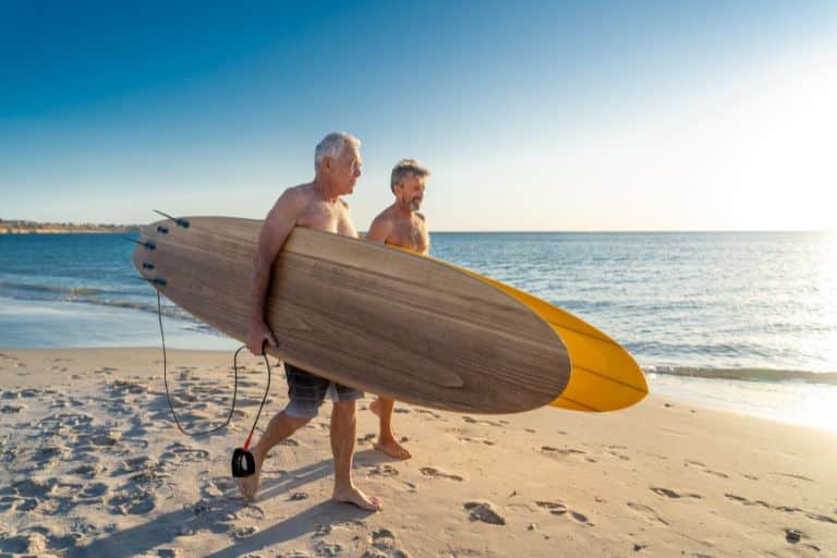 two over 50s retired men with surfboards going down to the bea ch together - join a community of retired people and live the lifestyle you want